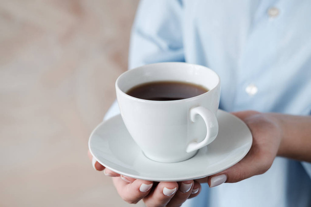Bir fincan kahve tutan kadın. Bej arka planda siyah çay fincan ile Kadın elleri. Yakın çekim - Fotoğraf, Görsel