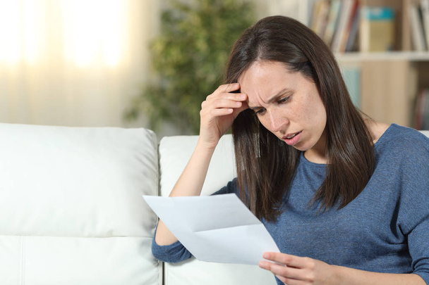 Worried woman reading a letter on a couch at home - Photo, Image