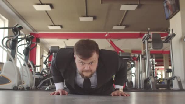 A male caucasian businessman in a black suit performs physical exercises in a gym, wring out of the floor and looks into the camera as a concept of a healthy lifestyle office workers - Video