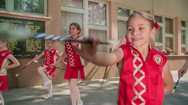 女の子は赤い衣装を着て、彼らのマジョレットスティックで練習しています。これは校庭で行われています. - 映像、動画