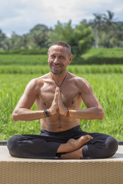 Man doing yoga and meditating in a position near a green rice terrace on the tropical island of Bali, Indonesia. Close up - Fotografie, Obrázek