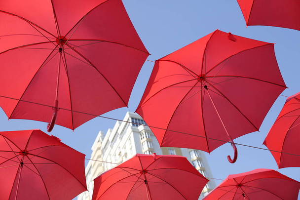 Rote Regenschirme gegen den blauen Himmel und das weiße Gebäude. abstrakter Hintergrund mit Regenschirmen - Foto, Bild