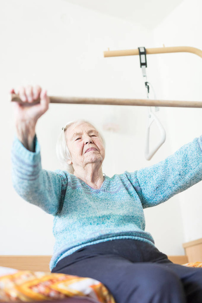 Ouderen 96 jaar oud vrouw oefenen met een stok zitten op haar slechte. - Foto, afbeelding