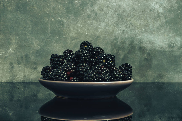 Fresh blackberry in bowl on a glass and gray wall background. - Foto, immagini
