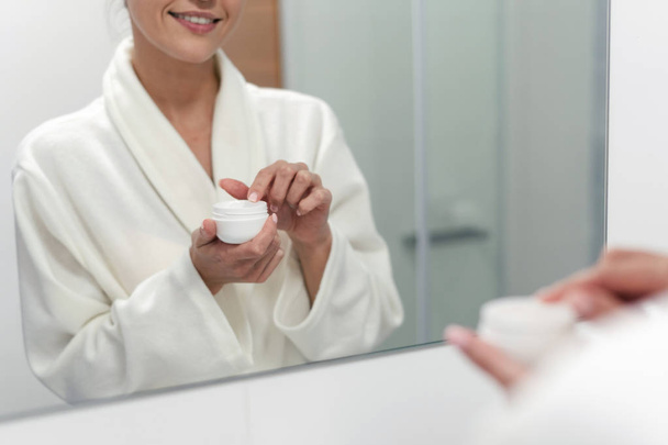 Femme tenant crème dans les mains, debout à la salle de bain
 - Photo, image