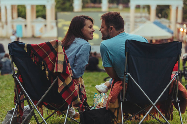 pareja sentada en sillas de campamento en el parque de la ciudad mirando la película al aire libre en el cine al aire libre
 - Foto, Imagen
