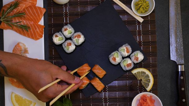 Served A Set Of Sushi With Salmon And Tuna, California Rolls, Maki, Soy Sauce Closeup On The Table. Eat sushi with chopsticks. Hands eat sushi with chopsticks. - 写真・画像