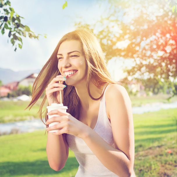 Beautiful happy young woman drinking coffee in park - Фото, изображение