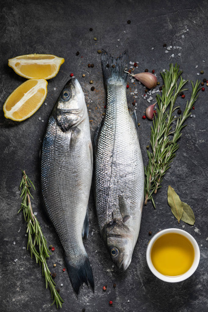 Fresh fish seabass and ingredients for cooking, lemon and rosemary. Dark background top view. - Foto, Imagem