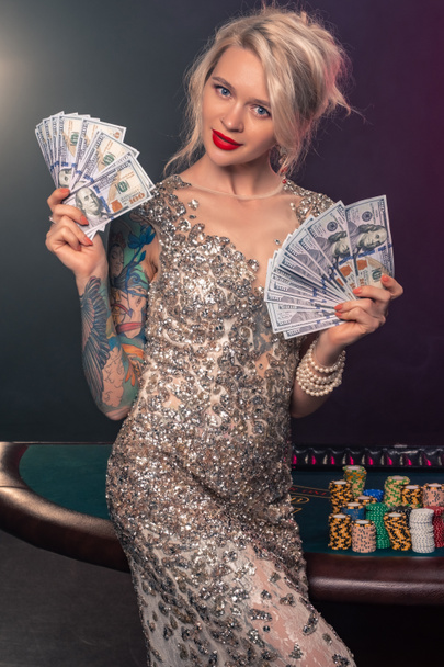 Blonde woman with a beautiful hairstyle and perfect make-up is posing with some money in her hands. Casino, poker. - Φωτογραφία, εικόνα