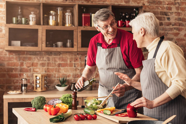 Senior man and woman laughing and preparing healthy food at kitchen - Fotografie, Obrázek