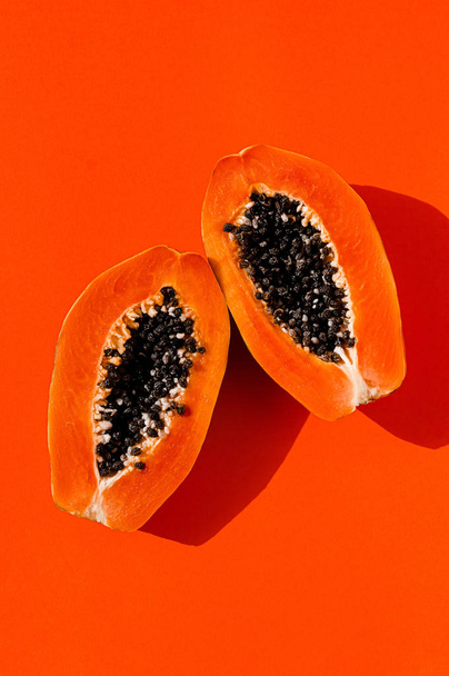 Φρέσκα παπάγια εξωτικά τροπικά φρούτα σε πορτοκαλί φόντο. Φωτισμός ηλιακής ημέρας. Μινιμαλιστική καλοκαιρινή επίπεδη ταπετσαρία. Δημιουργική ιδέα φαγητού. Αντιγραφή προτύπου χώρου. Έντονα χρώματα. - Φωτογραφία, εικόνα