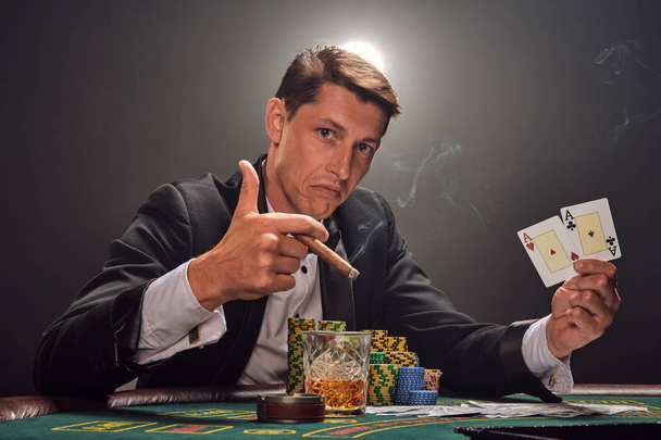 bel homme émotionnel joue au poker assis à la table dans le casino contre un projecteur blanc
. - Photo, image