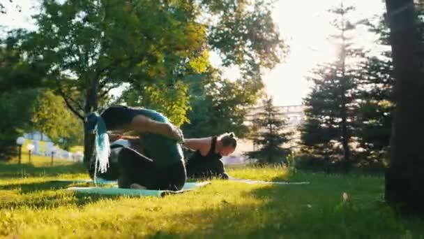 zwei junge Frauen bei Yoga-Übungen mit Trainer im Park im Sonnenlicht - eine Frau hat lange blaue Dreadlocks - Filmmaterial, Video