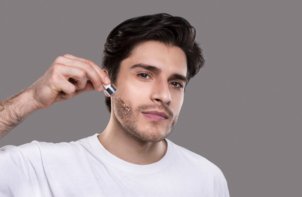 Young man applying organic essential serum on face - Foto, afbeelding