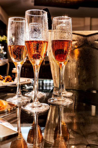 Glasses of champagne with frape and bottle in background, on table with reflection. - Foto, Imagen