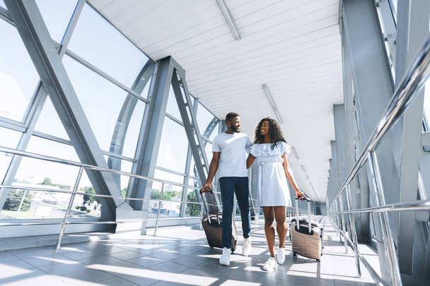 Щаслива чорна пара в повсякденному одязі, що йде в терміналі аеропорту з багажем
 - Фото, зображення