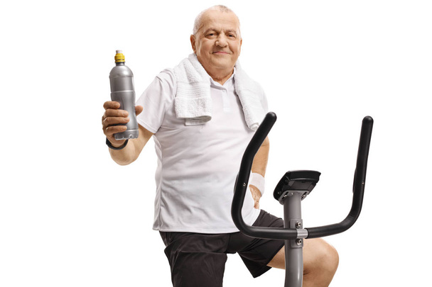 Mature man on an exercise bike holding a water bottle - Fotoğraf, Görsel
