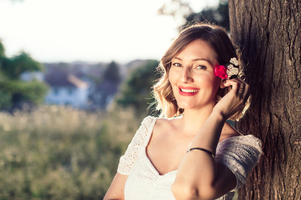 Gelukkige jonge dame met bloem rusten in zomerpark. Glimlachend breed met rode lippenstift op haar lippen. Womens dag concept - Foto, afbeelding