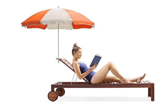 Young woman reading a book and relaxing on a sunbed under umbrel - Фото, изображение