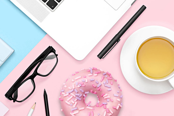 Flat lay photo of office desk with laptop notebook, glasses, sweet food donut and tea mug. Creative workspace on pastel color background - Photo, Image