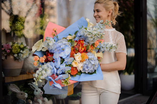 Woman holding a huge bouquet of tender light blue and orange color flowers - Фото, изображение