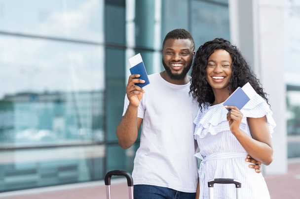 Африканская пара улыбается с авиабилетами и паспортами в аэропорту
 - Фото, изображение