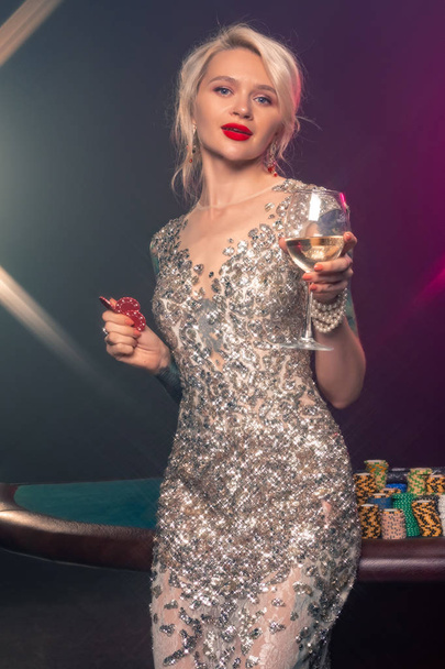 Die blonde Frau mit der schönen Frisur und dem perfekten Make-up posiert mit roten Glücksspielchips in den Händen. Casino, Poker. - Foto, Bild