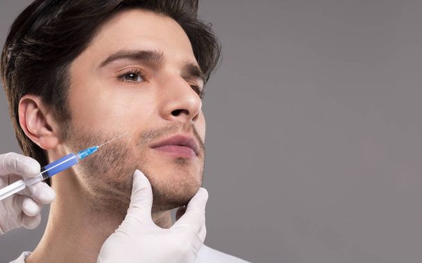 Esthéticienne faisant injection de beauté dans la mâchoire du patient masculin
 - Photo, image