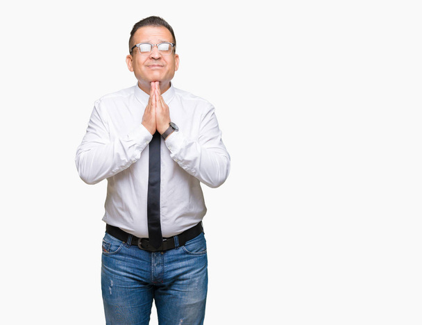 Geschäftsleute mittleren Alters arabischer Mann mit Brille vor isoliertem Hintergrund beten mit den Händen zusammen und bitten um Vergebung lächeln zuversichtlich. - Foto, Bild
