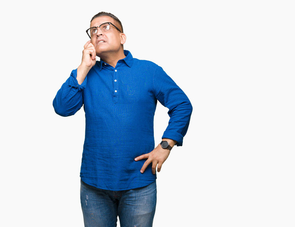 Middle age arab man wearing glasses over isolated background with hand on chin thinking about question, pensive expression. Smiling with thoughtful face. Doubt concept. - Fotoğraf, Görsel