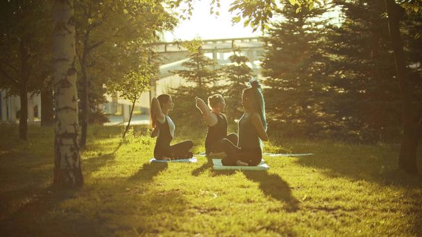 Két fiatal nő és egy férfi, aki jóga a parkban a sugarai az esti nap - Fotó, kép
