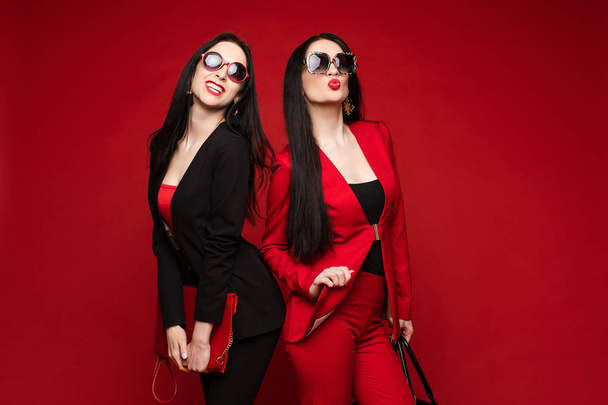 Due giovani moda elegante modello femminile in occhiali da sole sorridente posa isolata a studio rosso
 - Foto, immagini