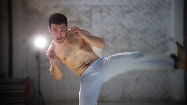 Nuori urheilullinen mies tekee capoeira-harjoituksia kääntämällä ja nostamalla jalka sitten hän toistaa liikkeitä
 - Materiaali, video