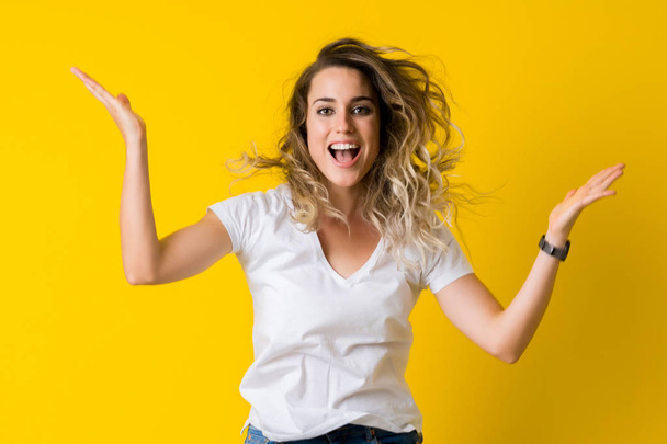 Mooie jonge blonde vrouw springen blij en opgewonden over geïsoleerde gele achtergrond - Foto, afbeelding