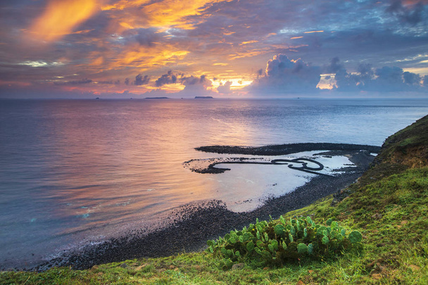 colina verde en la orilla del océano con cielo nublado puesta de sol
 - Foto, Imagen