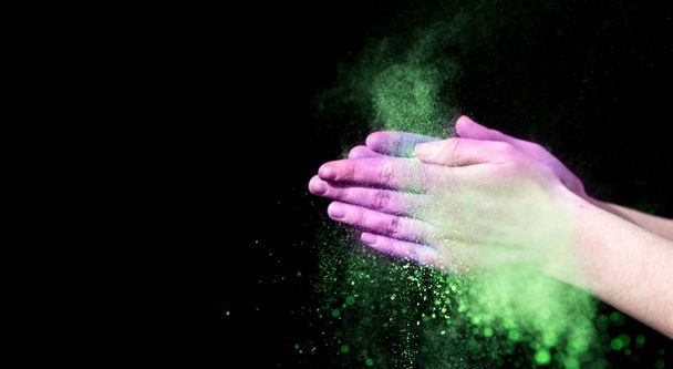 Colorful powder in clapping hands on black background - Fotoğraf, Görsel