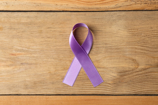 Purple ribbon on brown wooden background, top view. Domestic violence awareness - Fotó, kép