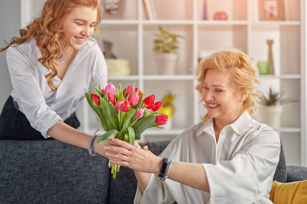 Cheerful young woman giving flowers to mother - Фото, изображение
