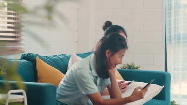 Young Lesbian lgbtq Asian women couple using mobile phone at home. Asian lover female happy relax fun using technology check social media in internet together while lying sofa in living room concept. - Filmmaterial, Video