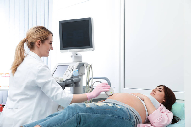 Young pregnant woman undergoing ultrasound scan in modern clinic - Фото, изображение