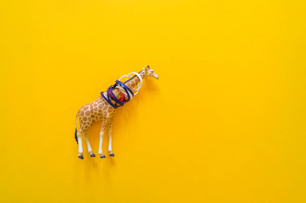 African animal giraffe in plastic. Suffering from garbage. Yellow background. - Фото, изображение