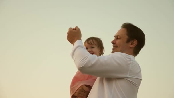Dad dancing on his shoulders with his daughter in sun. Father travels with baby on his shoulders in rays of sunset. A child with parents walks at sunset. happy family resting in park. family concept - Footage, Video