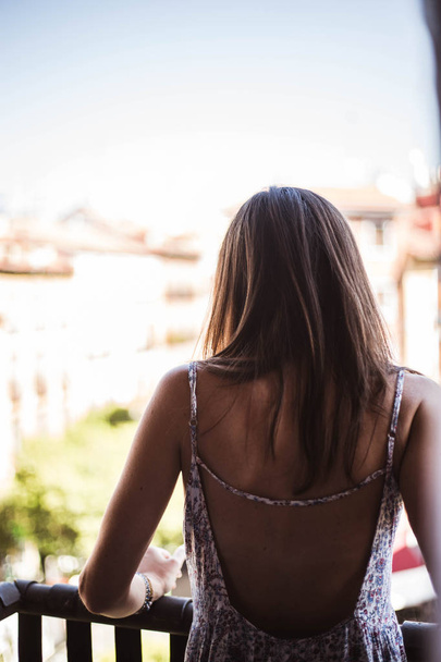 Back of young beautiful woman standing back in the balcony looking down on street in Madrid, Spain - 写真・画像
