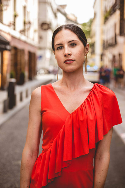 Portrait of beautiful brunette young woman with topknot hairstyle wearing red ruffles dress walking on the street. Fashion photo. - Foto, Imagem