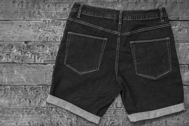 Black and white image of denim shorts with cuffs on wooden background. Fashionable unisex clothing. - Photo, Image