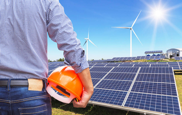 Caballete de ingeniero que sostiene casco amarillo de seguridad con células solares y turbinas eólicas que generan electricidad en la estación de sistemas de centrales híbridas
  - Foto, imagen