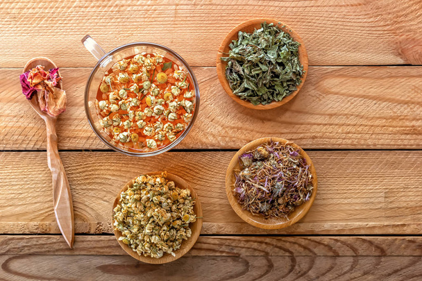 Herbal tea with pharmaceutical chamomile, dry chrysanthemum and hunters on a wooden table. View from above. - Photo, Image