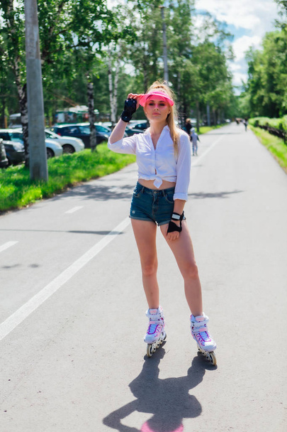 Portrait of an emotional girl in a pink cap visor and protective gloves for rollerblades and skateboarding riding on rollerblades on the road. - Valokuva, kuva
