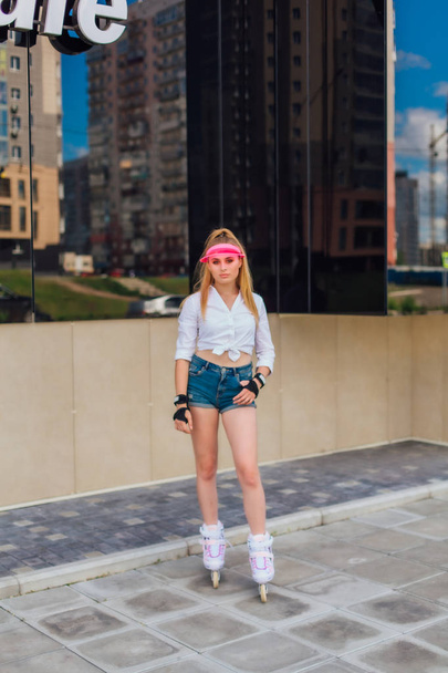 Portrait of an emotional girl in a pink cap visor and protective gloves for rollerblades and skateboarding riding on rollerblades on the road. - Fotó, kép